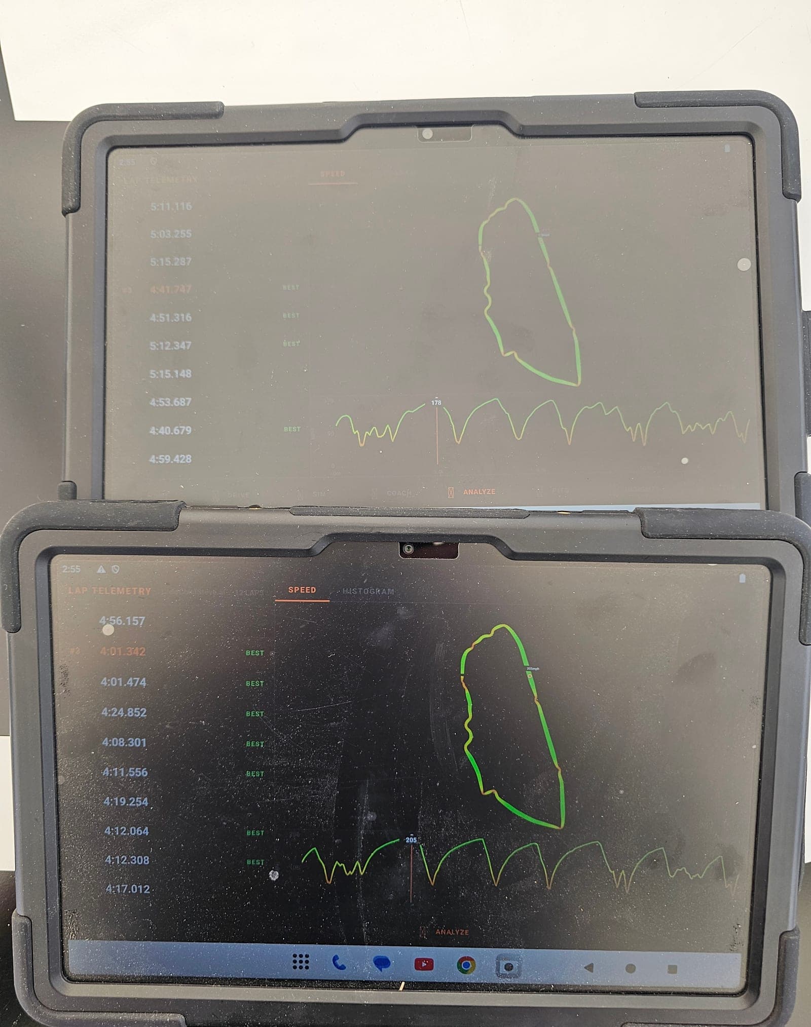 Two Mission Control Pads side by side in direct sun at the Le Mans Classic, both showing lap telemetry with speed traces reaching 205 mph
